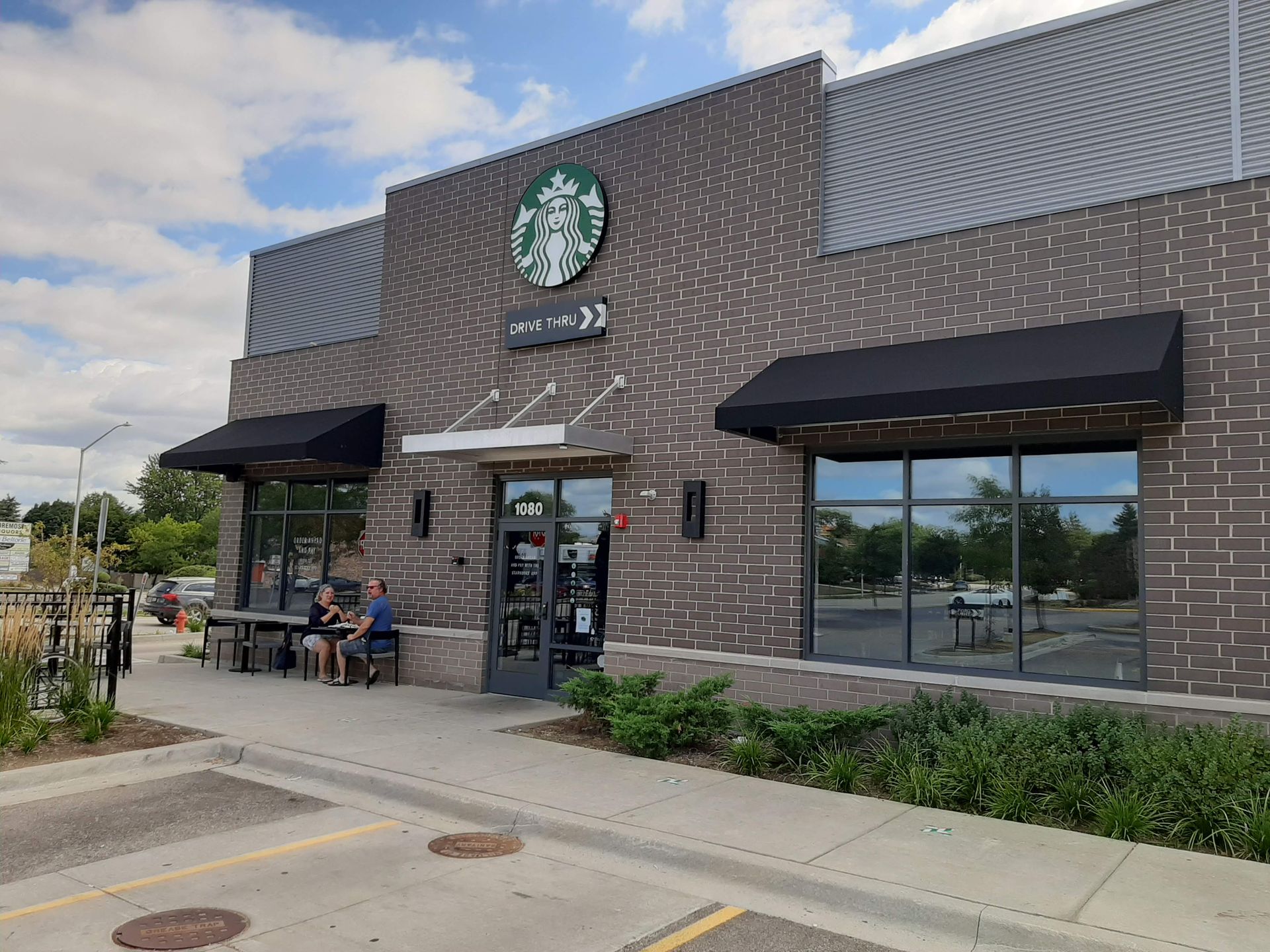 A starbucks coffee shop with people sitting at tables outside.