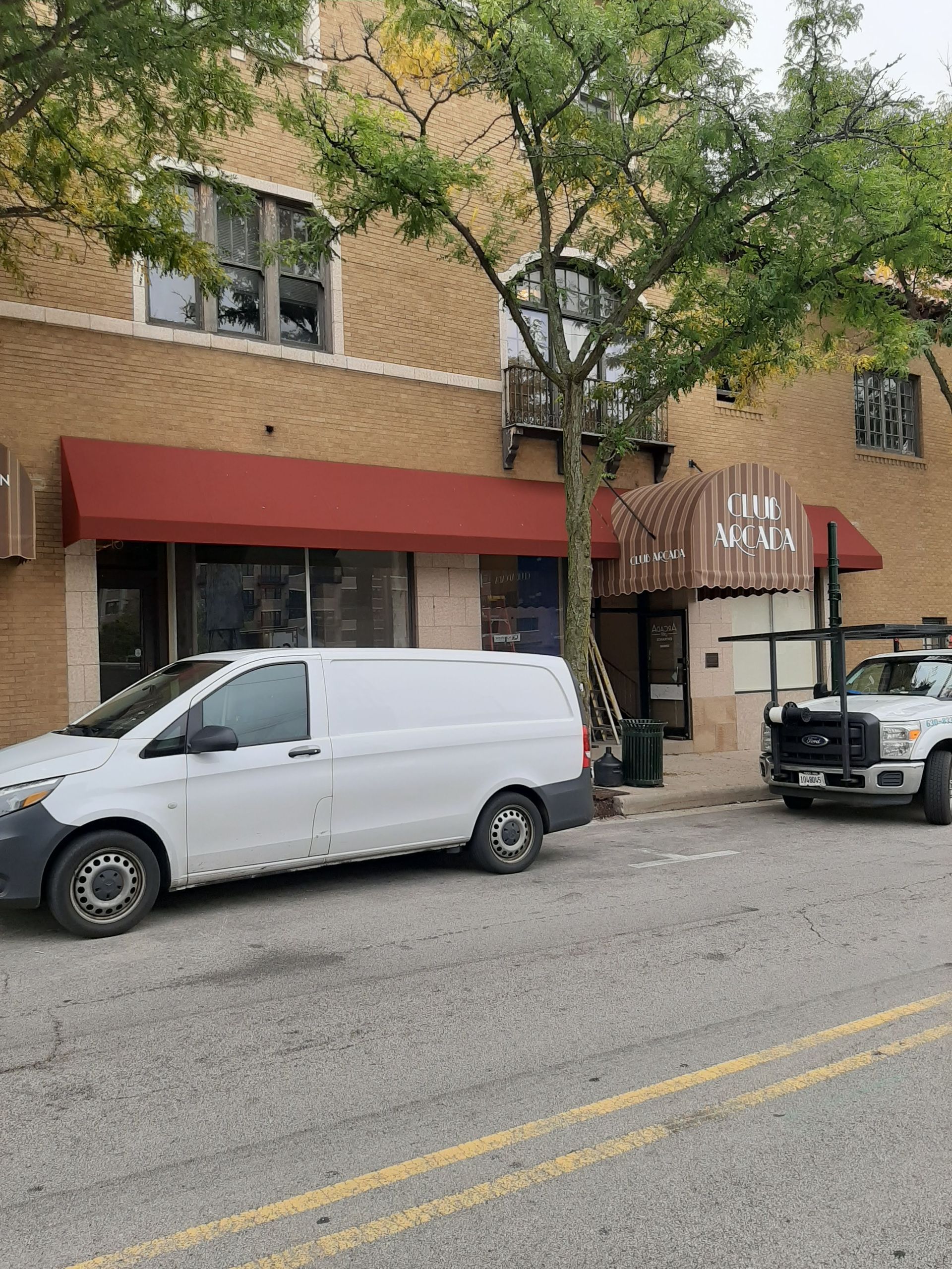 A white van is parked in front of a building with a red awning.