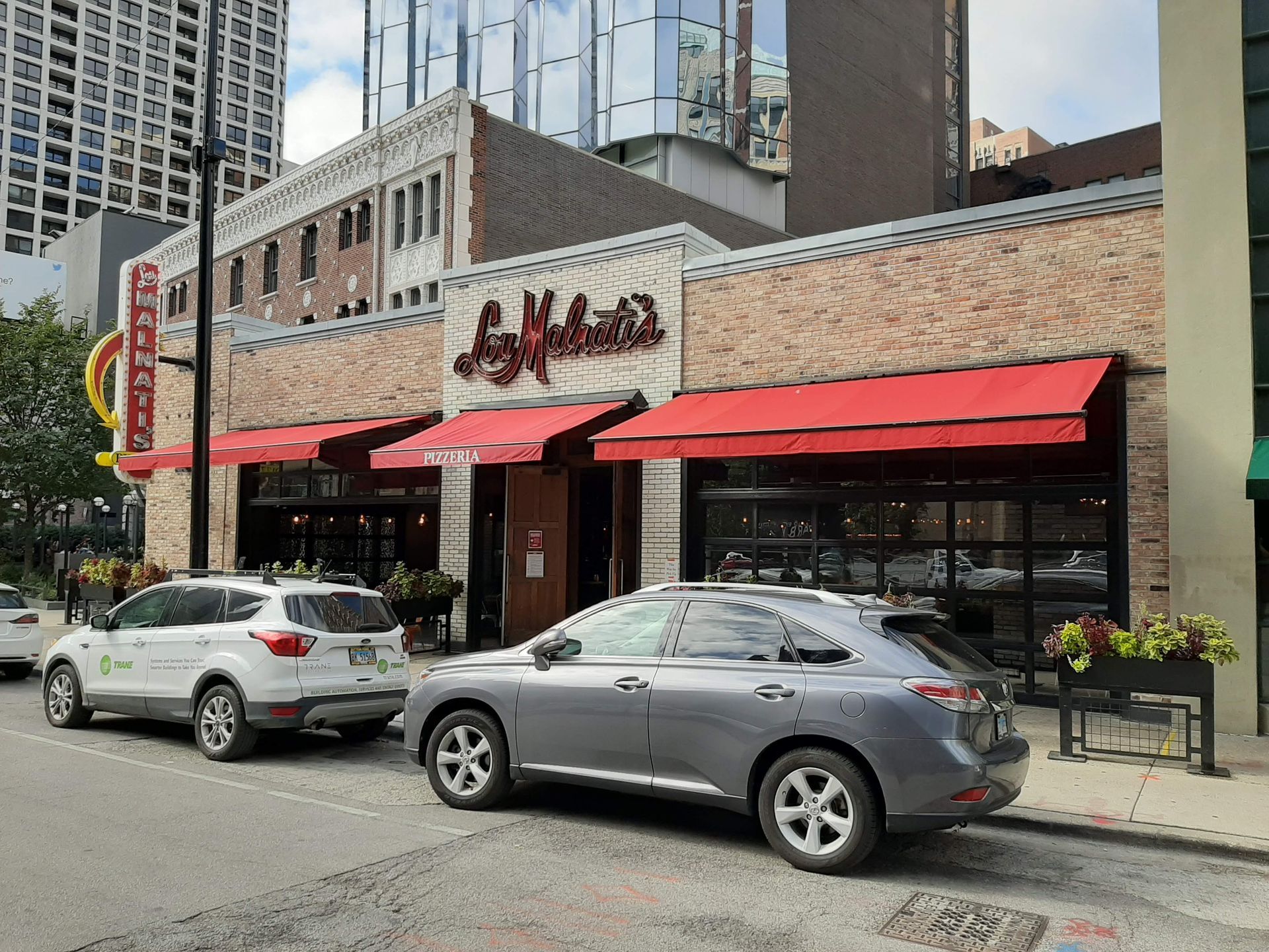 Two cars are parked in front of a restaurant with red awnings.