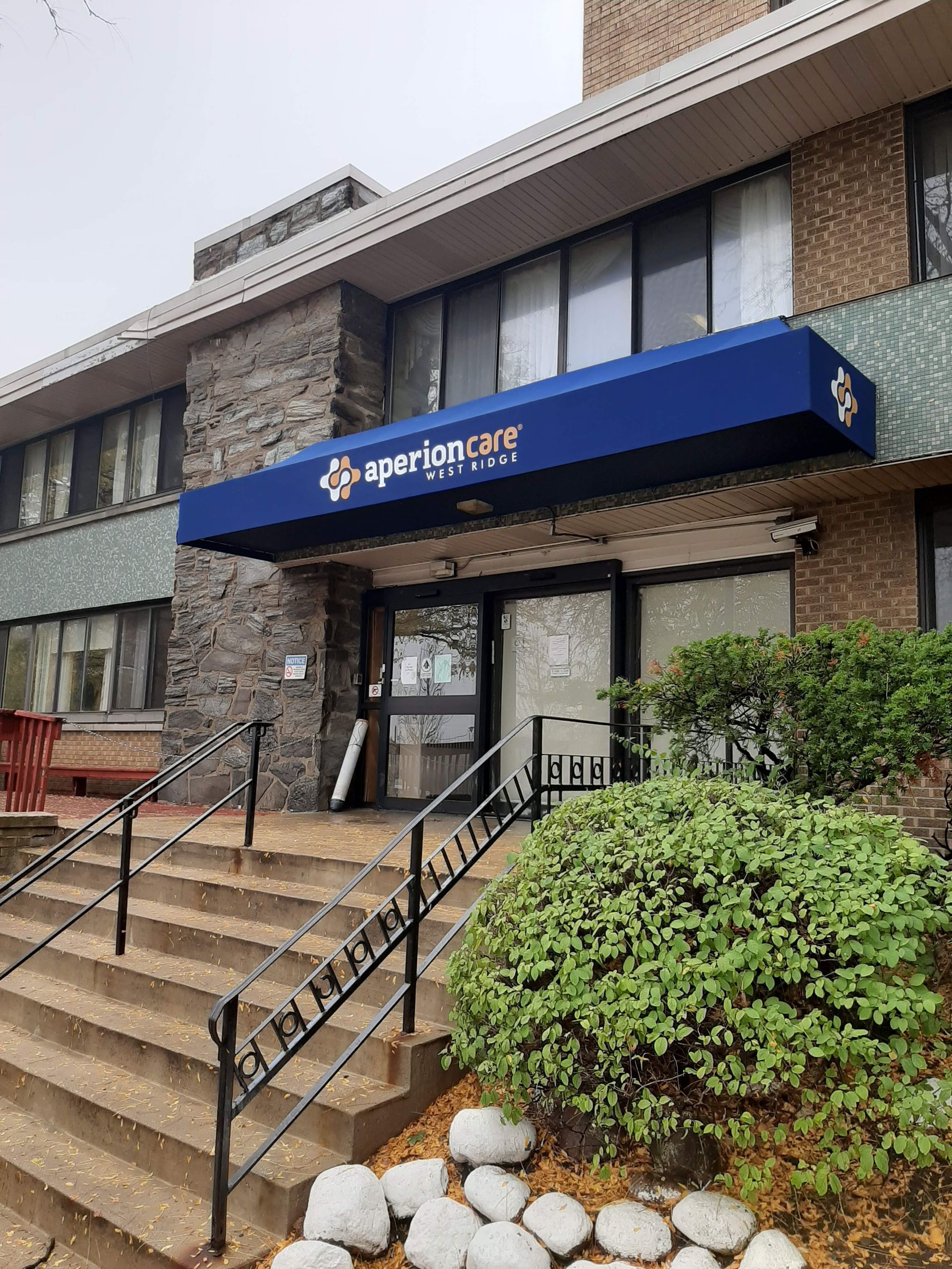 The front of a building with stairs and a blue awning.