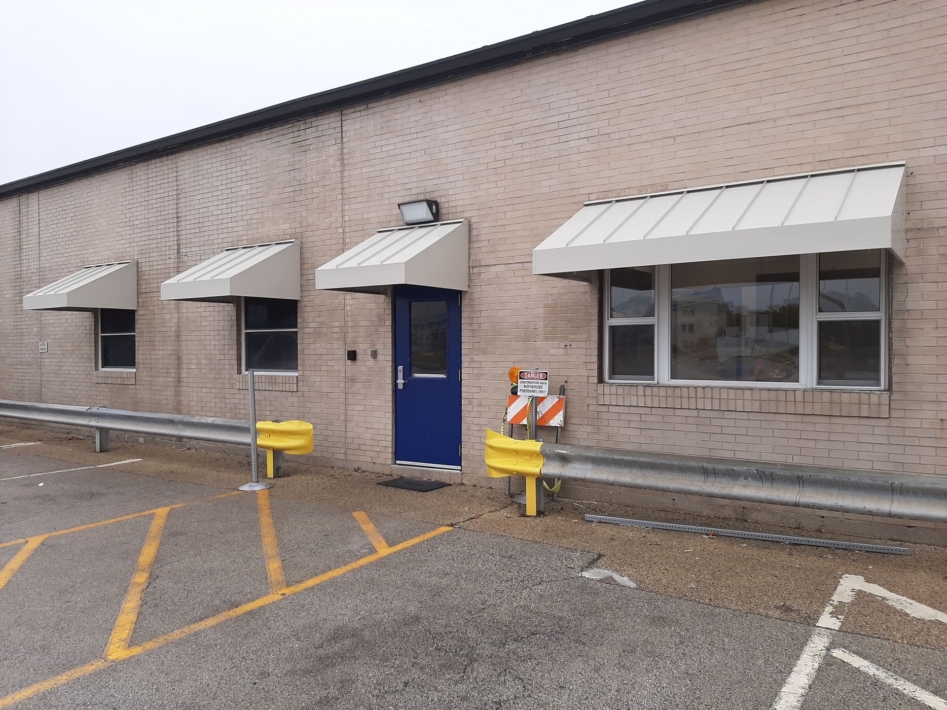 A brick building with a blue door and white awnings on the windows.