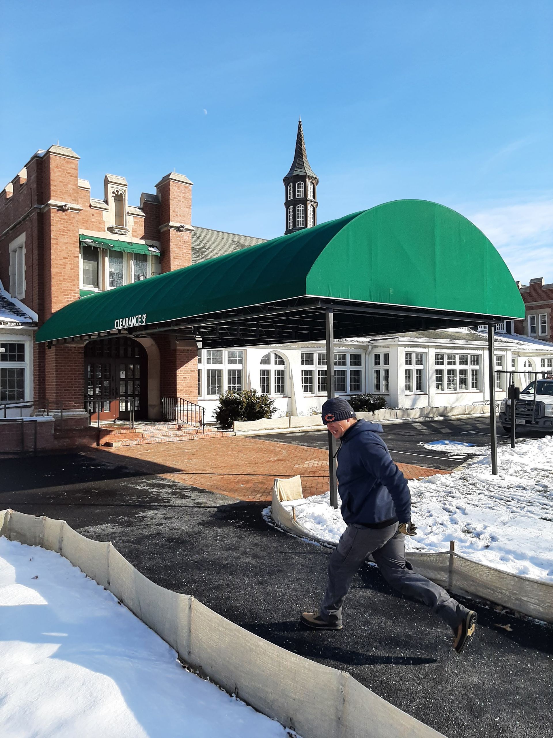 A man walking under a green awning in front of a building