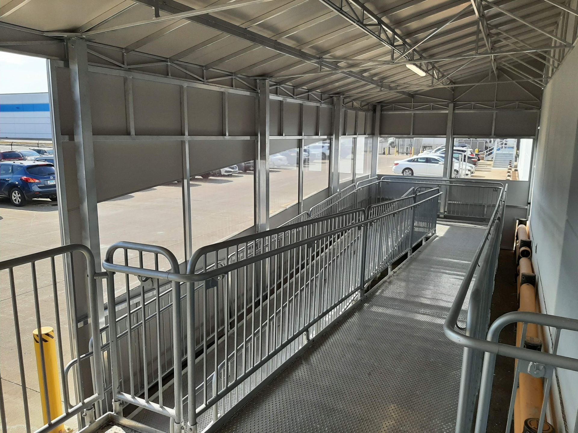 A covered walkway with a ramp and a railing leading to a parking lot.