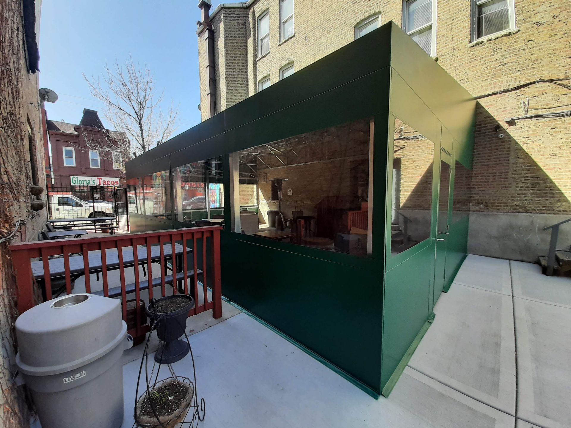 A patio with a green canopy and a trash can in front of a building.
