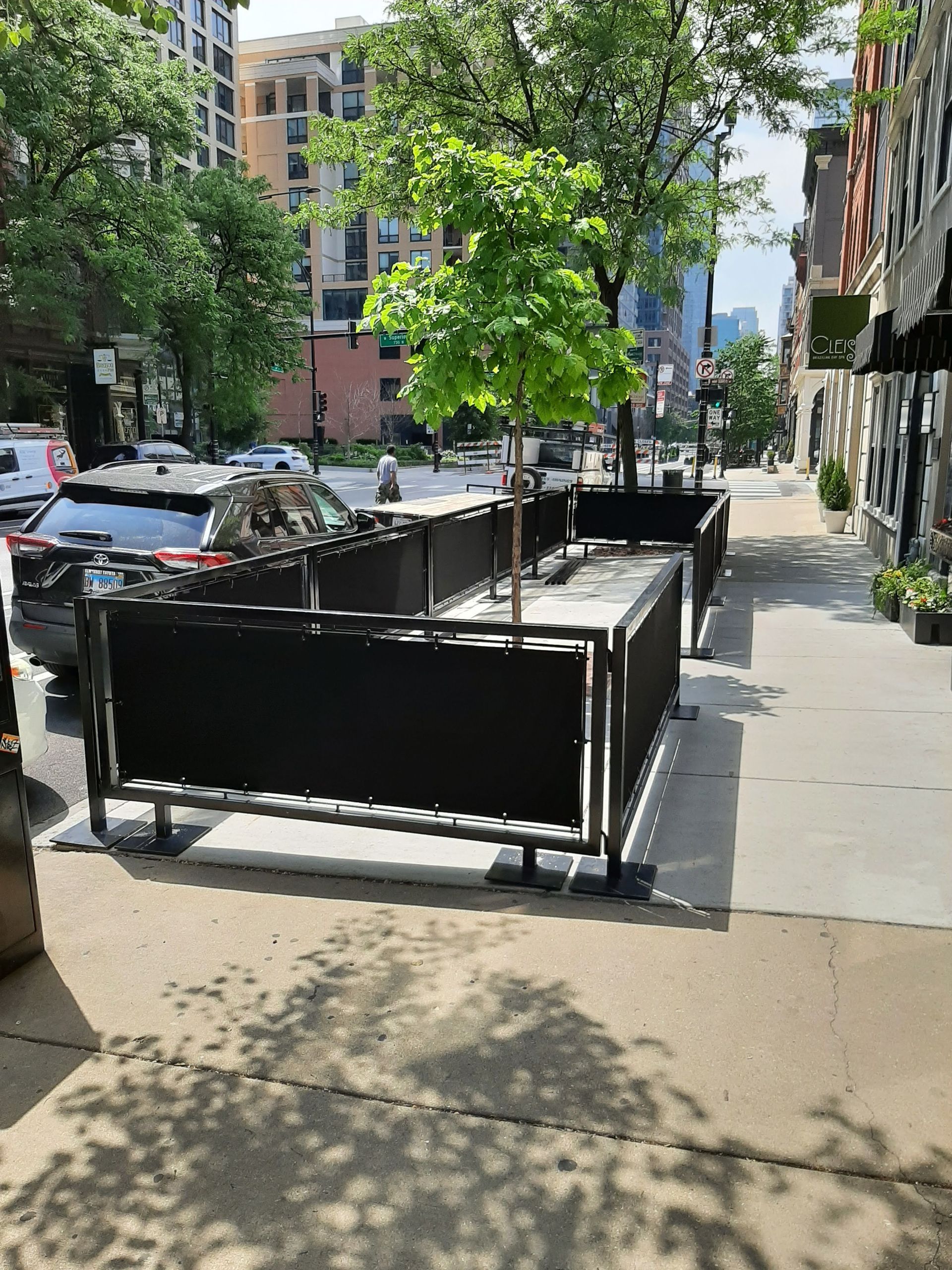 A sidewalk with a black fence and a tree in the middle of it.