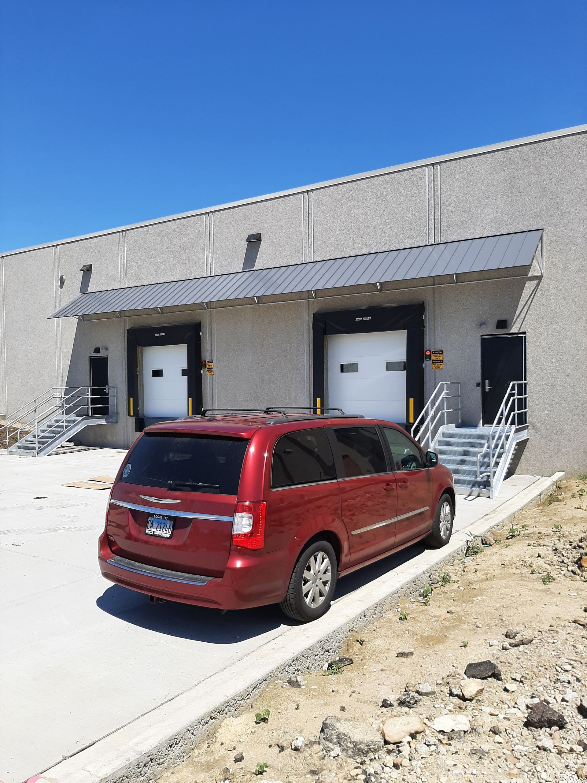 A red minivan is parked in front of a warehouse.