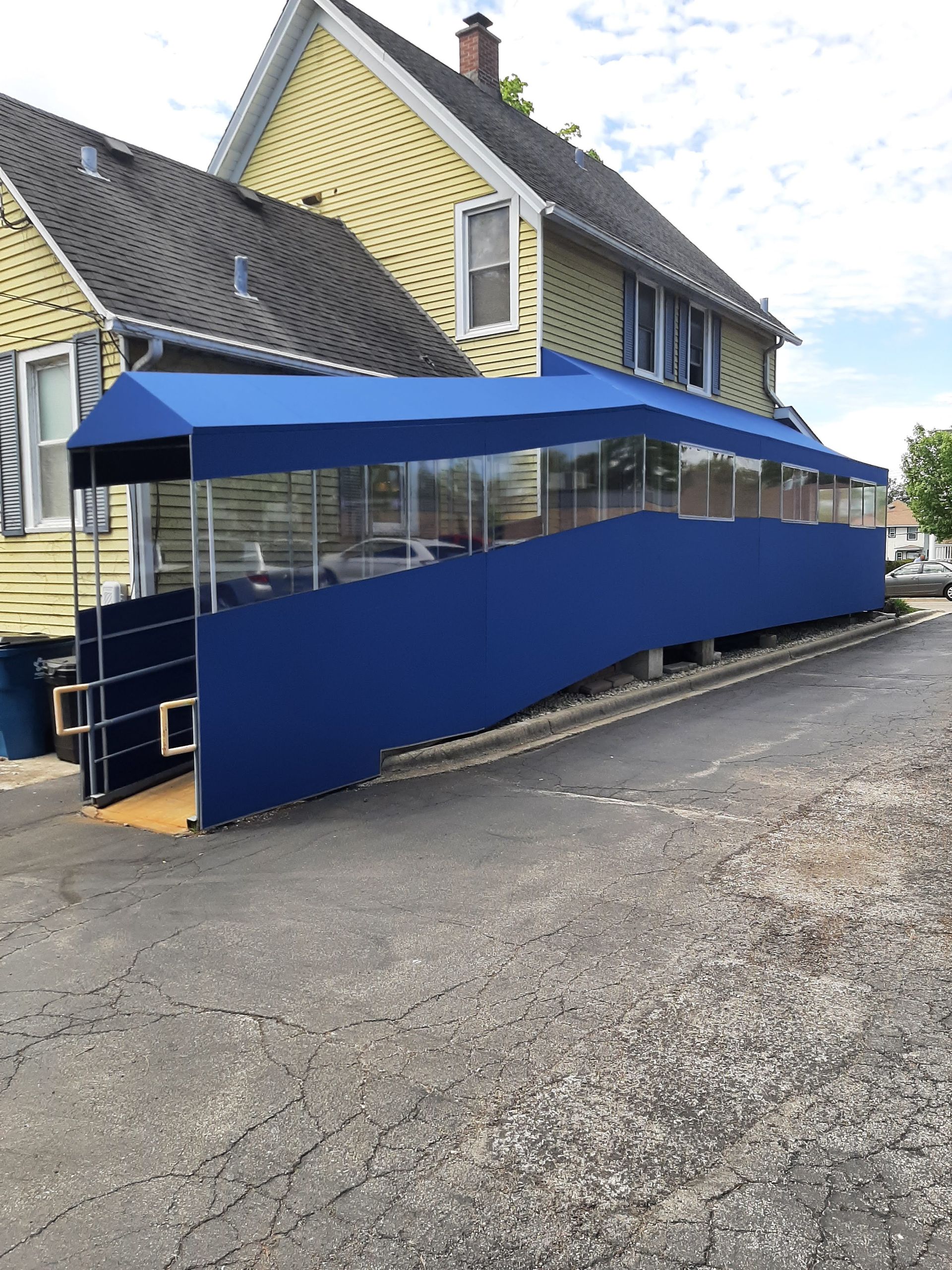 A blue awning is sitting in front of a yellow house.