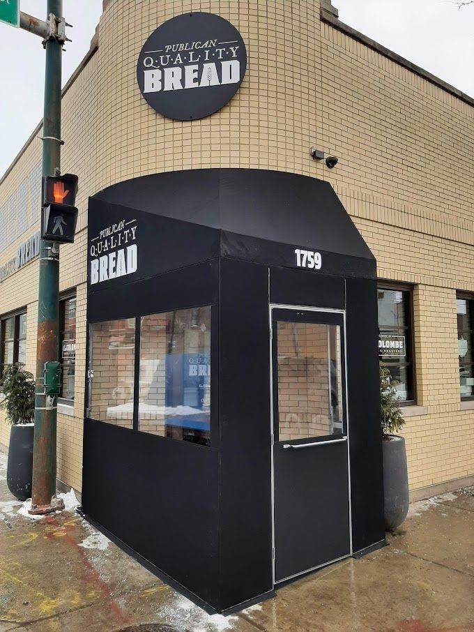 A brick building with a black awning that says quality bread