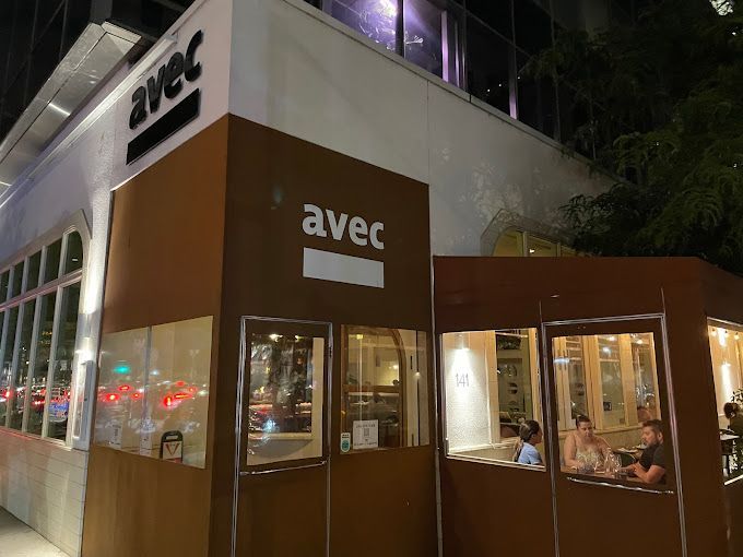 A group of people are sitting outside of a restaurant called avec.
