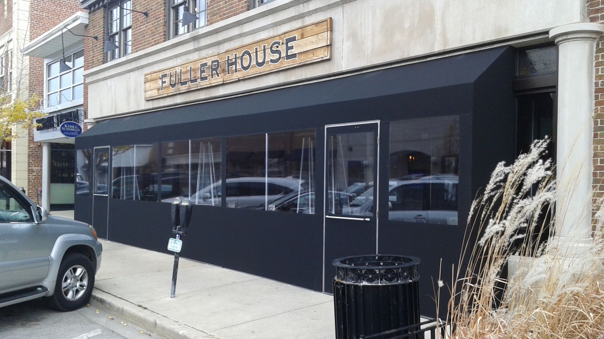 A car is parked in front of a restaurant with a black awning.