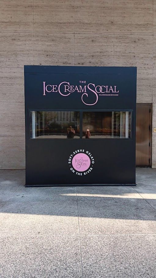 A black sign that says `` ice cream social '' is sitting on the sidewalk in front of a building.