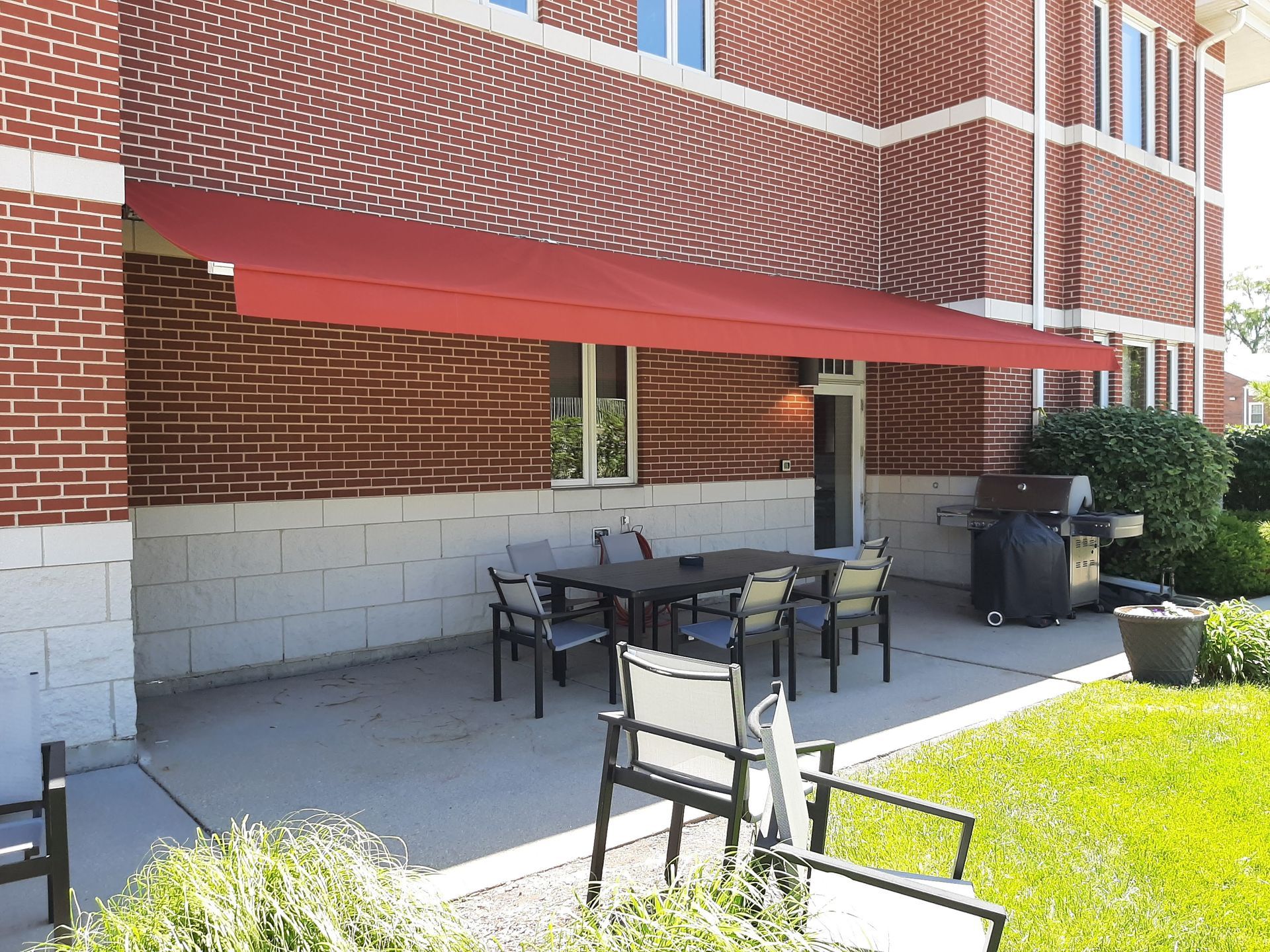 A brick building with a red awning over a patio with a table and chairs.