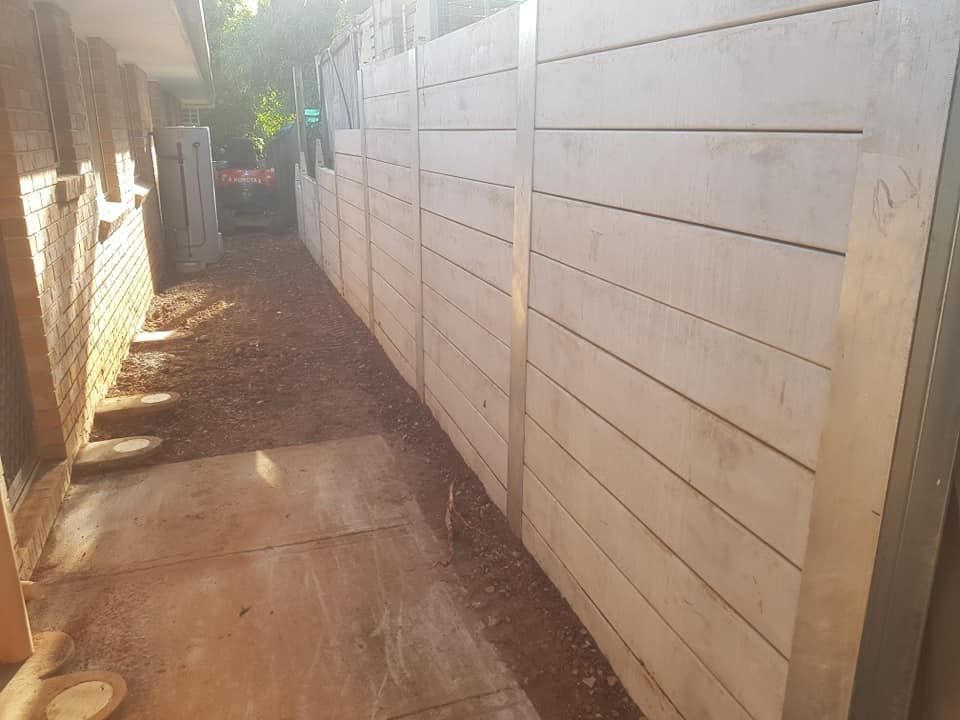 Concrete retaining wall along a pathway with brown soil.