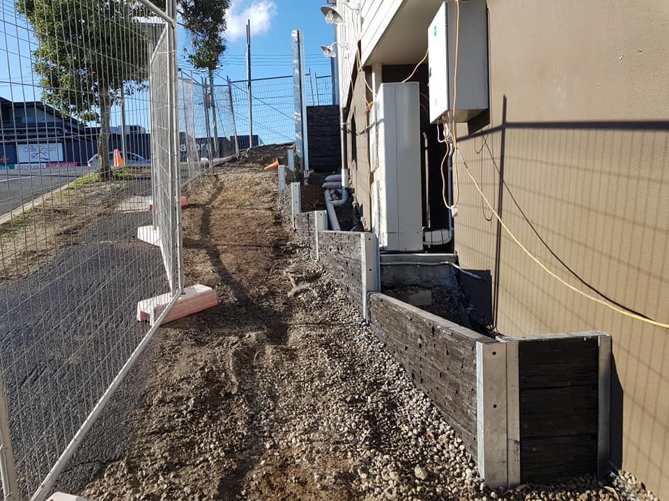 Construction site with fence, retaining walls, dirt path next to building.