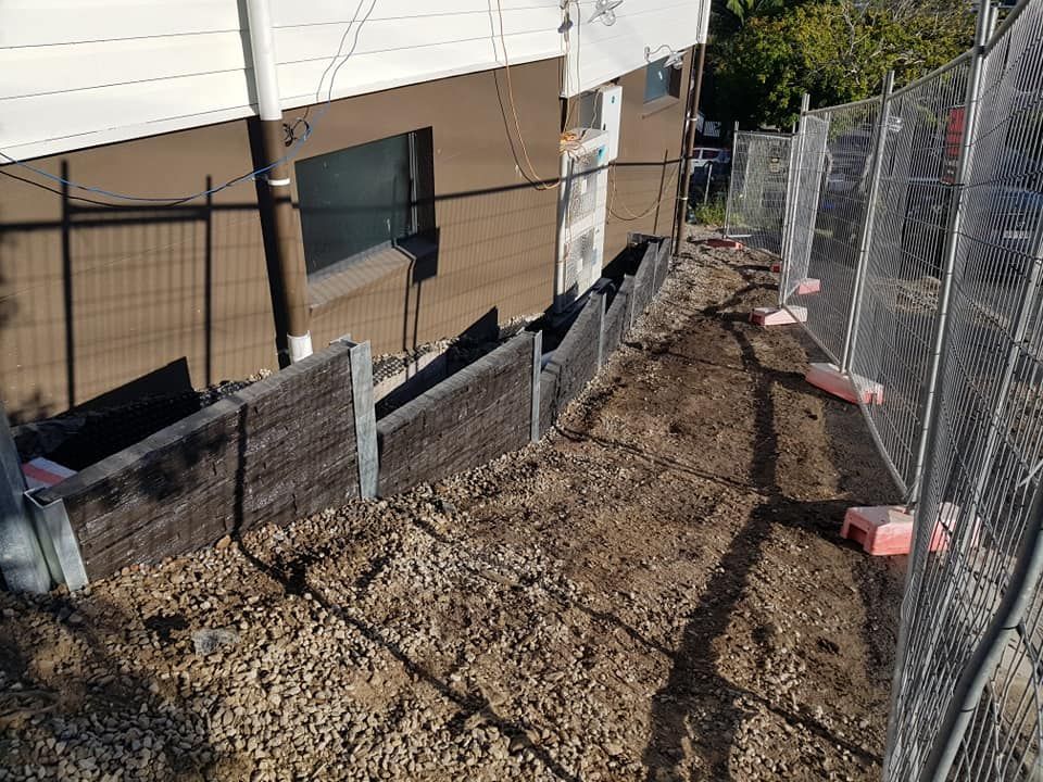 Dirt path alongside a building, enclosed by fencing, with wooden retaining walls.