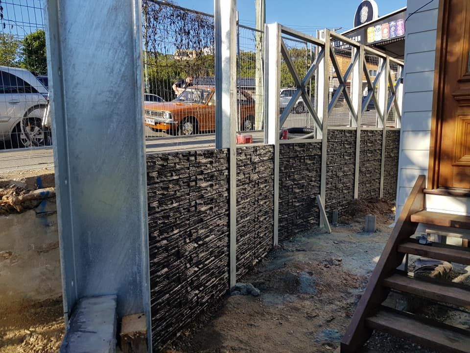Section of decorative stone and metal fence under construction with a wooden staircase.