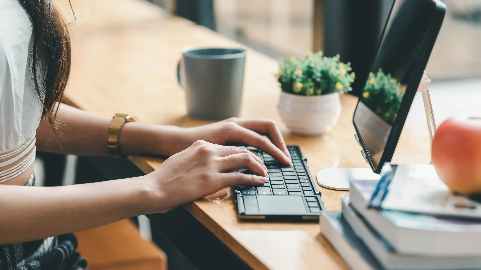 A woman is typing on a laptop computer at a desk.