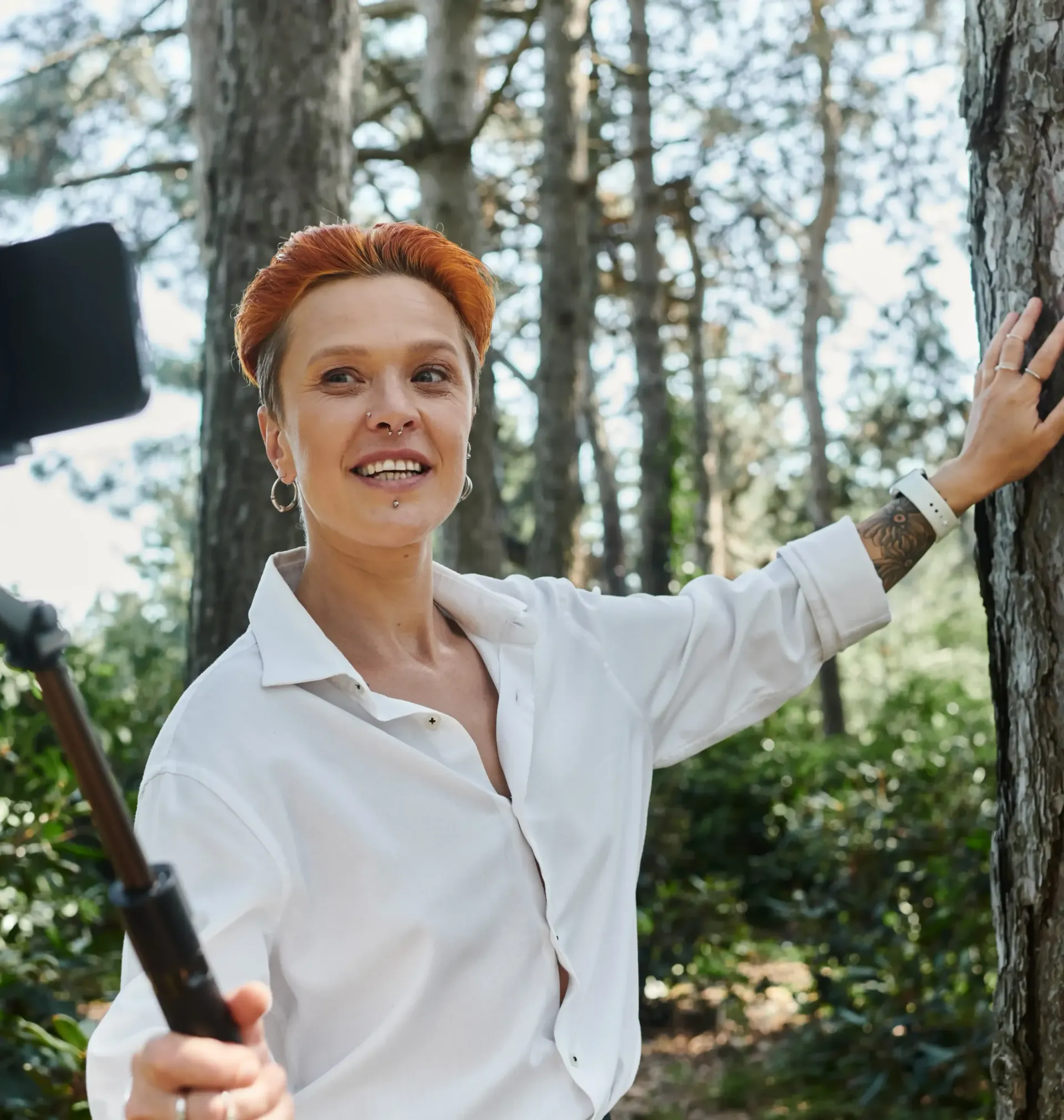 A woman in a white shirt is taking a selfie in the woods