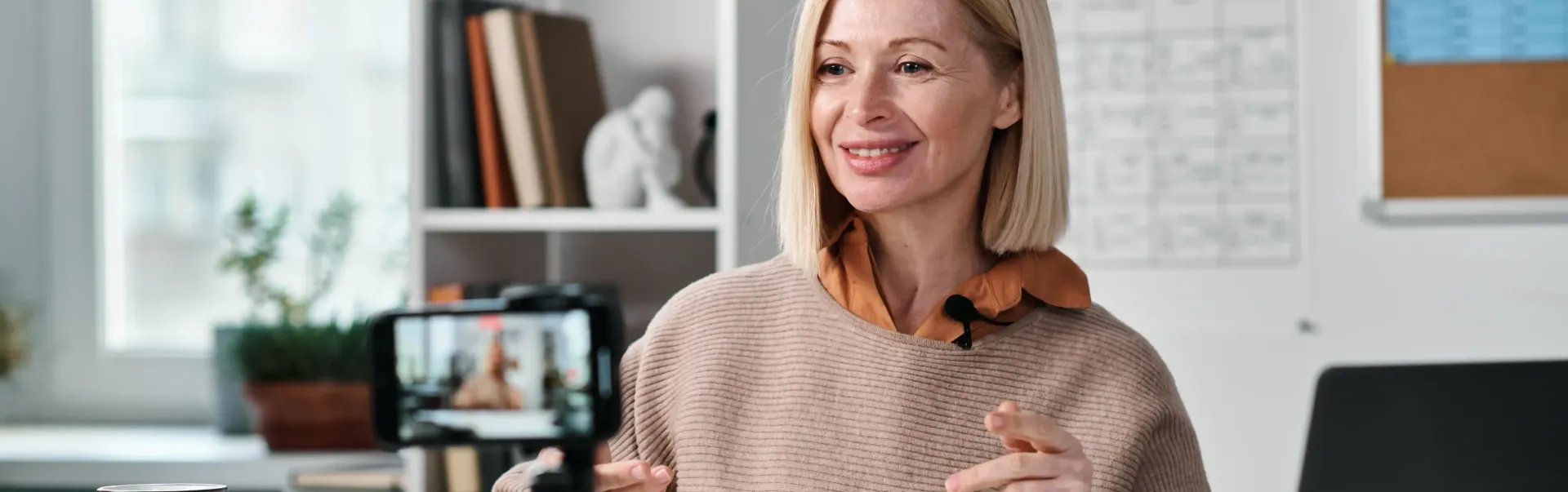 A woman is recording a video with a microphone on her phone for her masterclass.