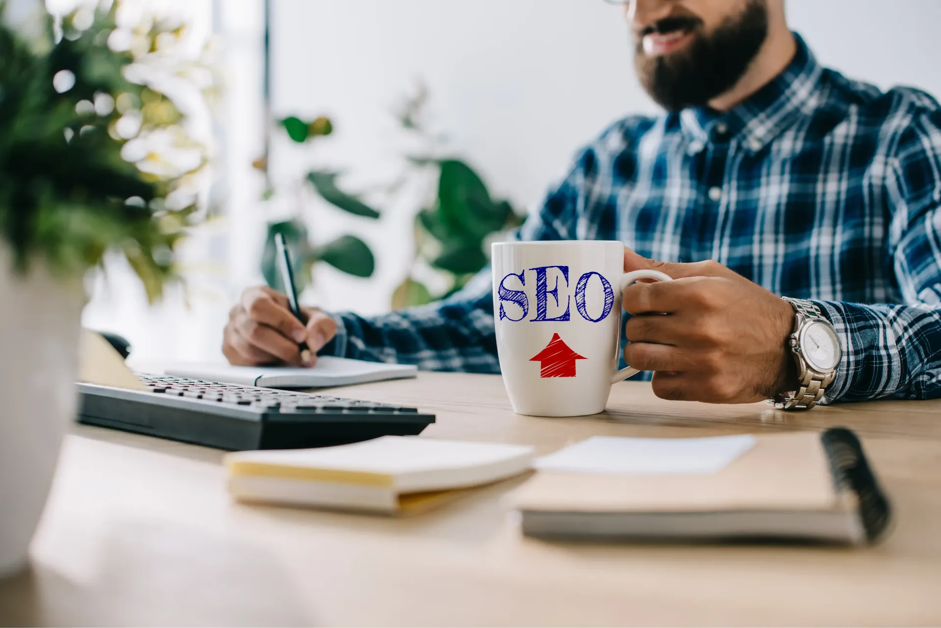 A man is sitting at a desk holding a mug that says seo.