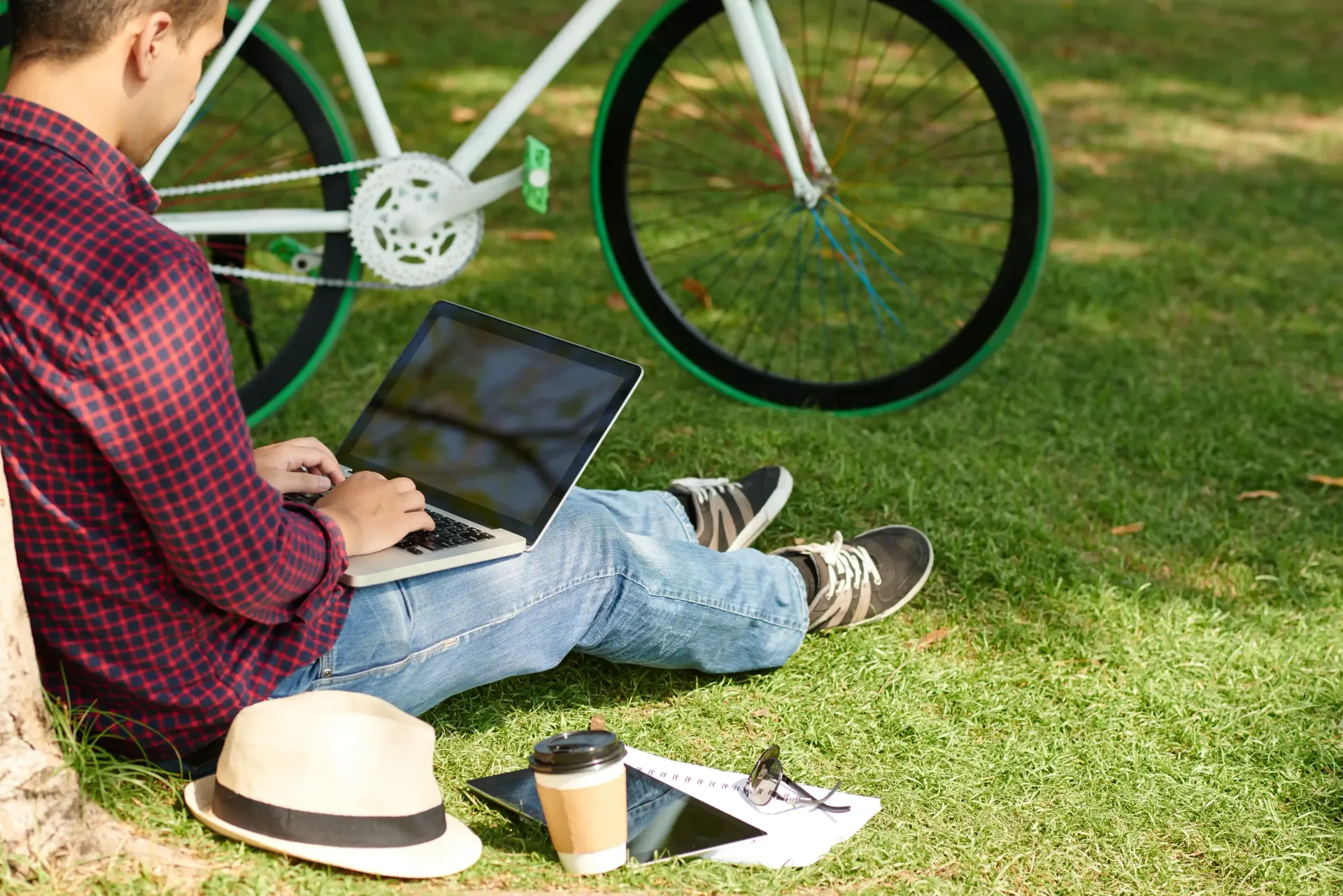 A full-time content creator is sitting on the grass with a laptop and a bicycle in the background.