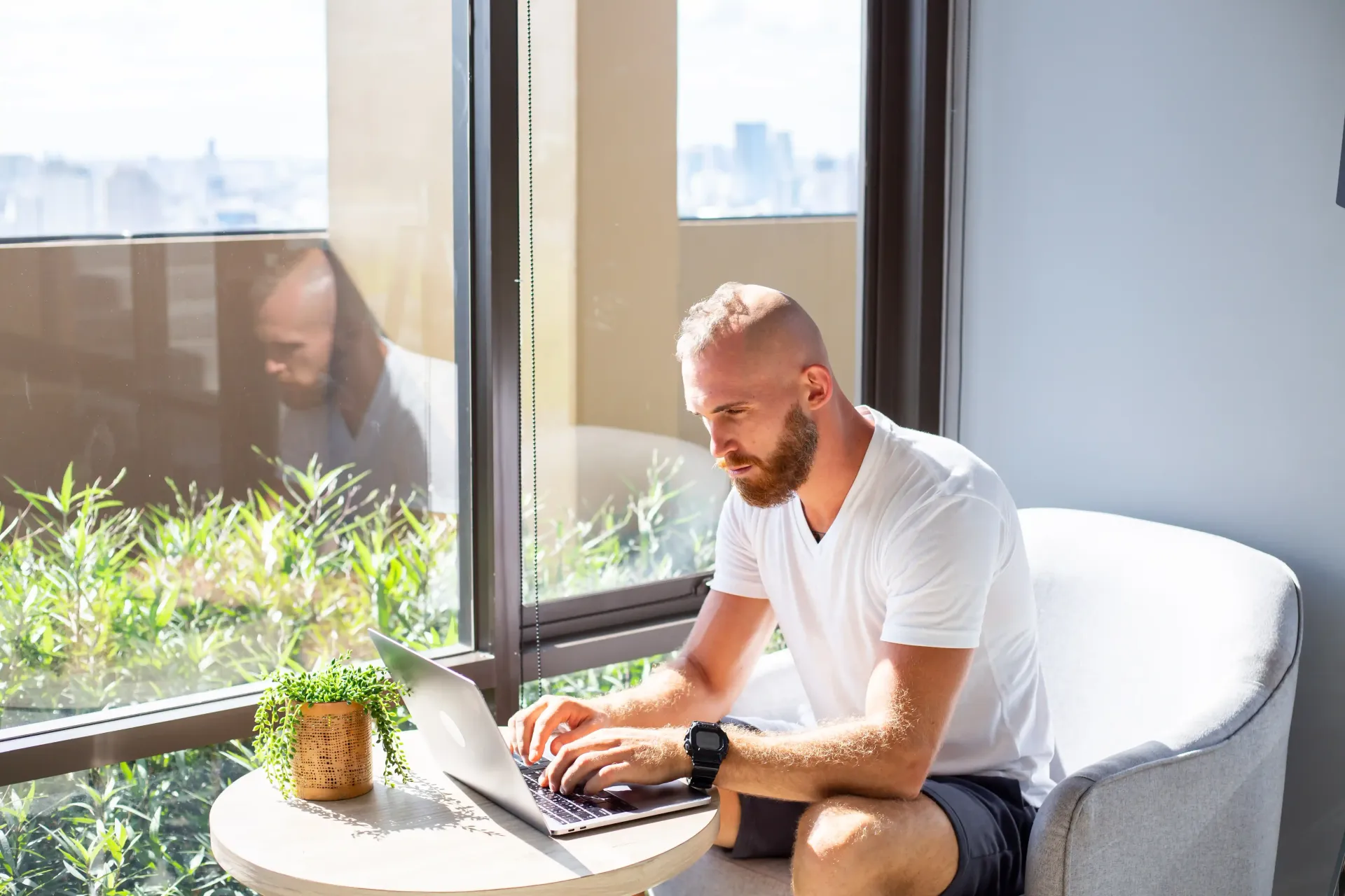 A man is sitting on a couch using a laptop computer for SEO to gain more AI visibility for his coaching business.