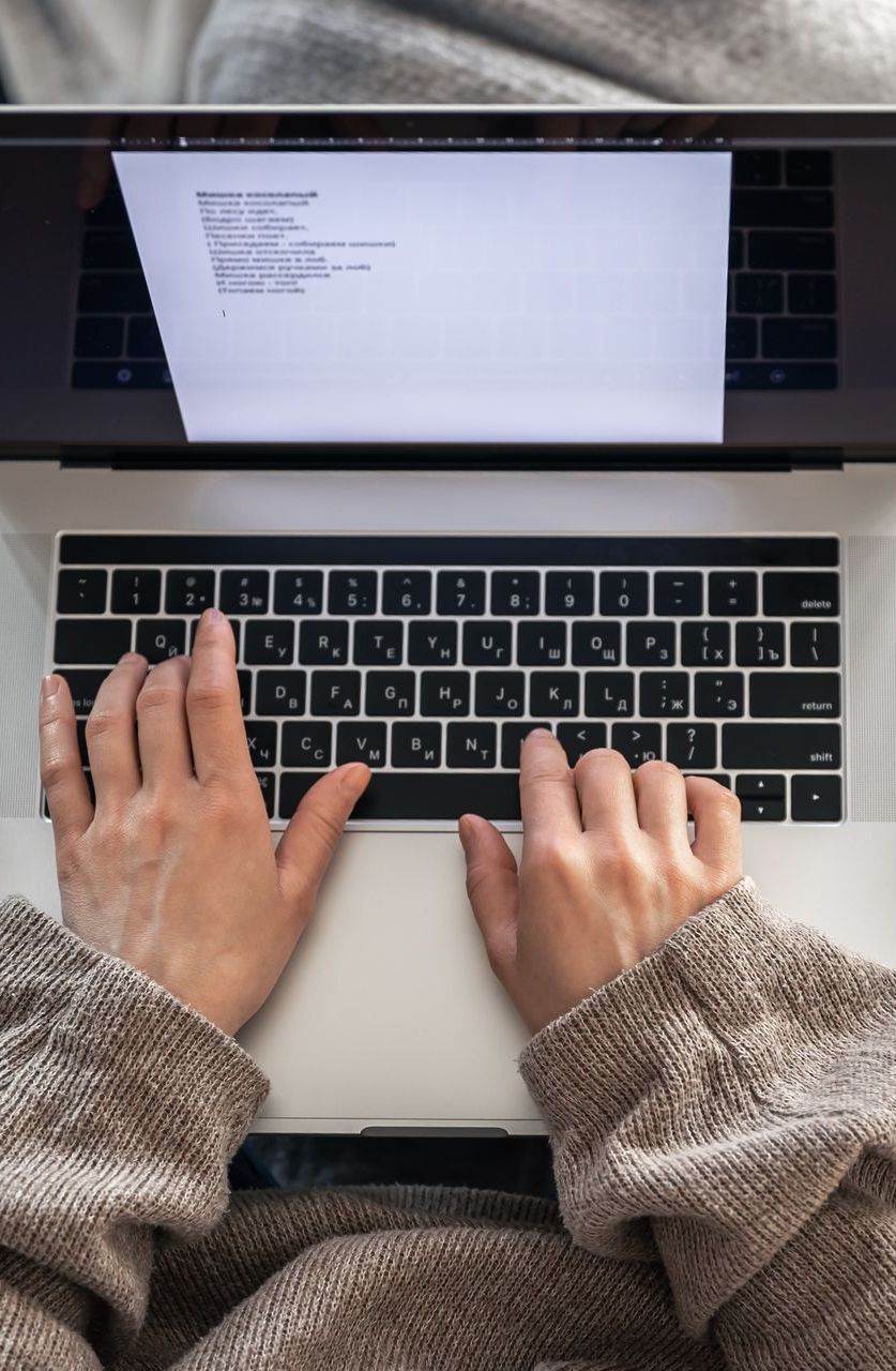 A person is typing on a laptop computer creating evergreen content.