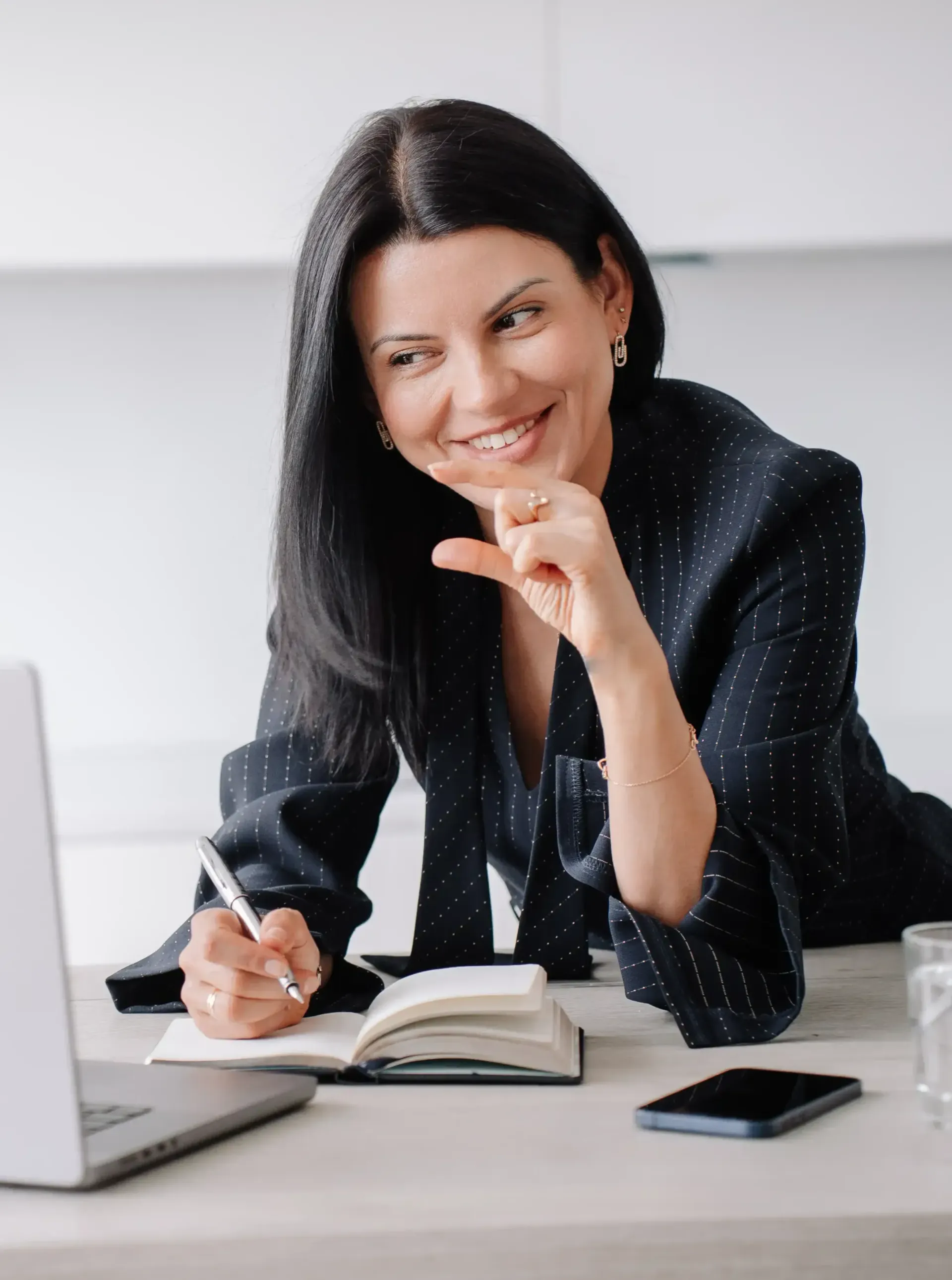 A woman is sitting at a desk with a laptop and a notebook coaching clients.