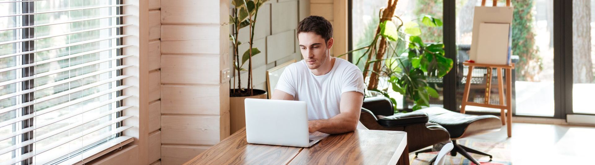A man is sitting at a table using a laptop computer to coach his clients.