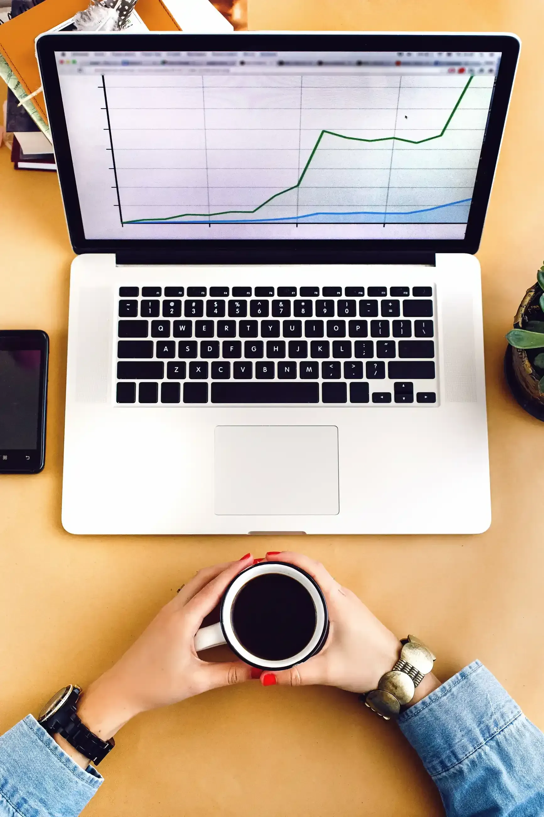 A person is holding a cup of coffee in front of a laptop computer.