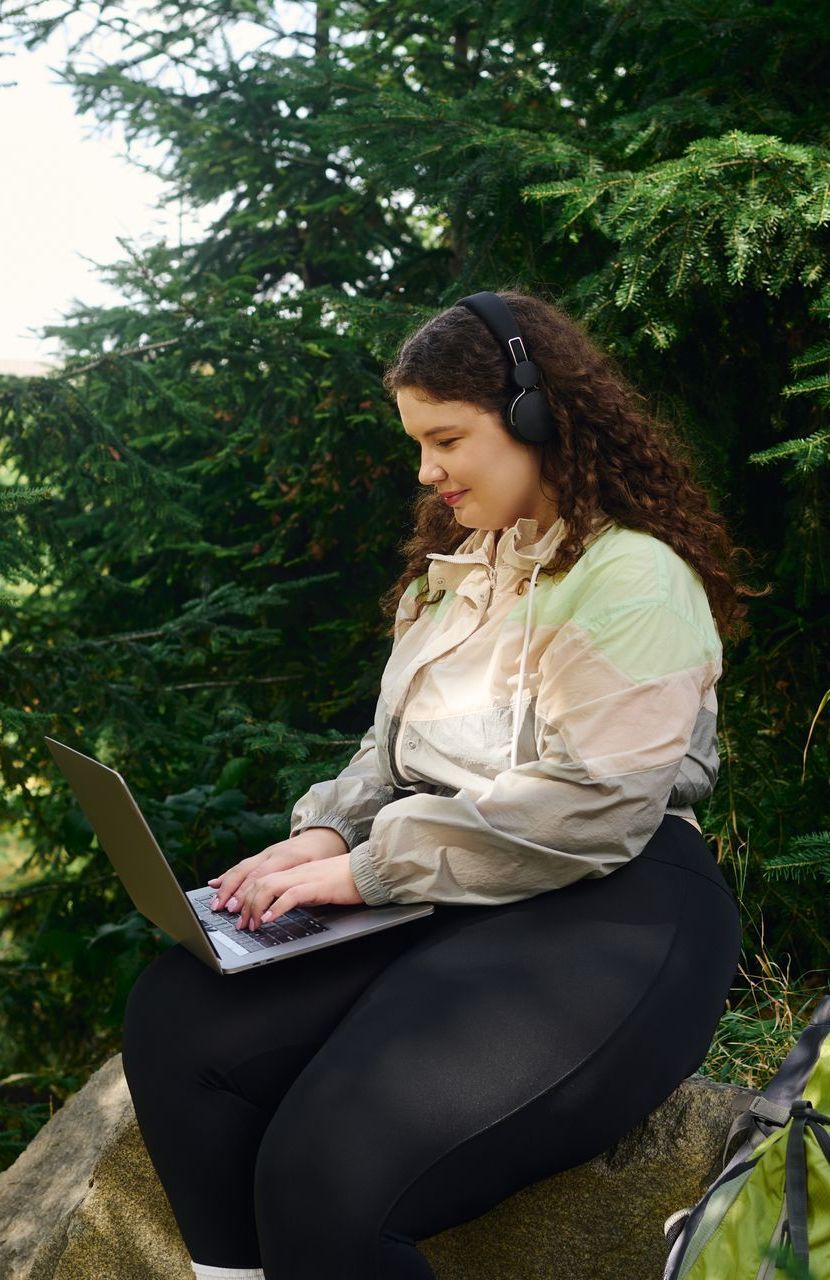 A woman is sitting on a rock using a laptop computer to create evergreen content.
