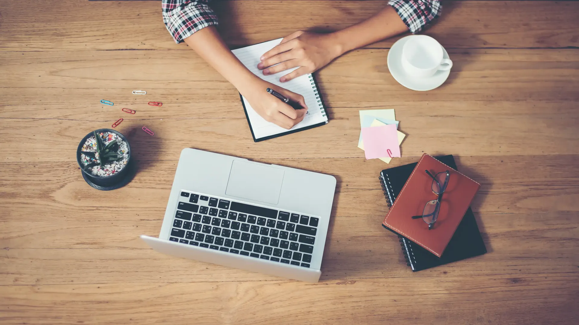 A person is sitting at a wooden table with a laptop and a cup of coffee.