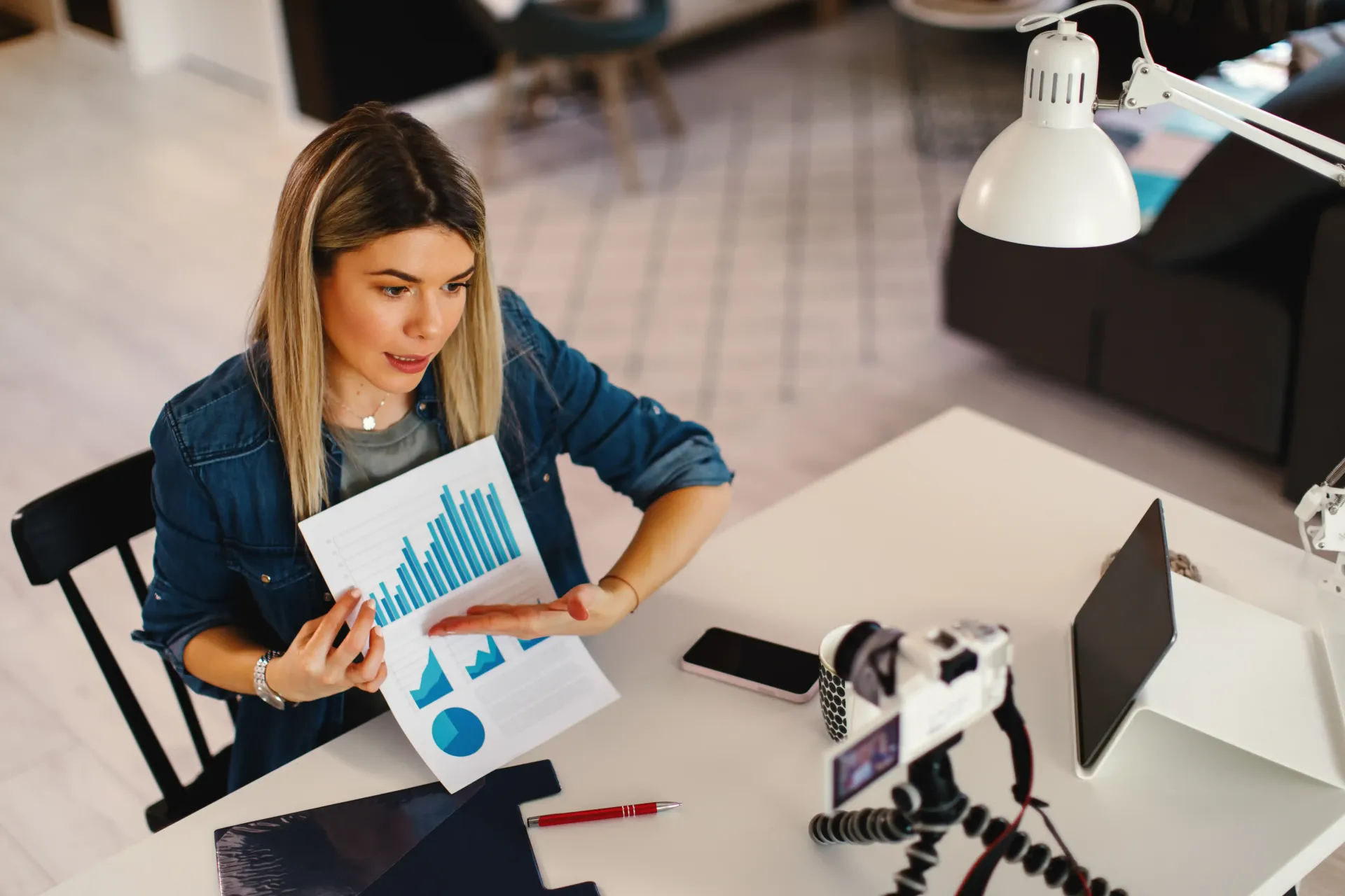 A woman is sitting at a desk holding a piece of paper with a graph on it.