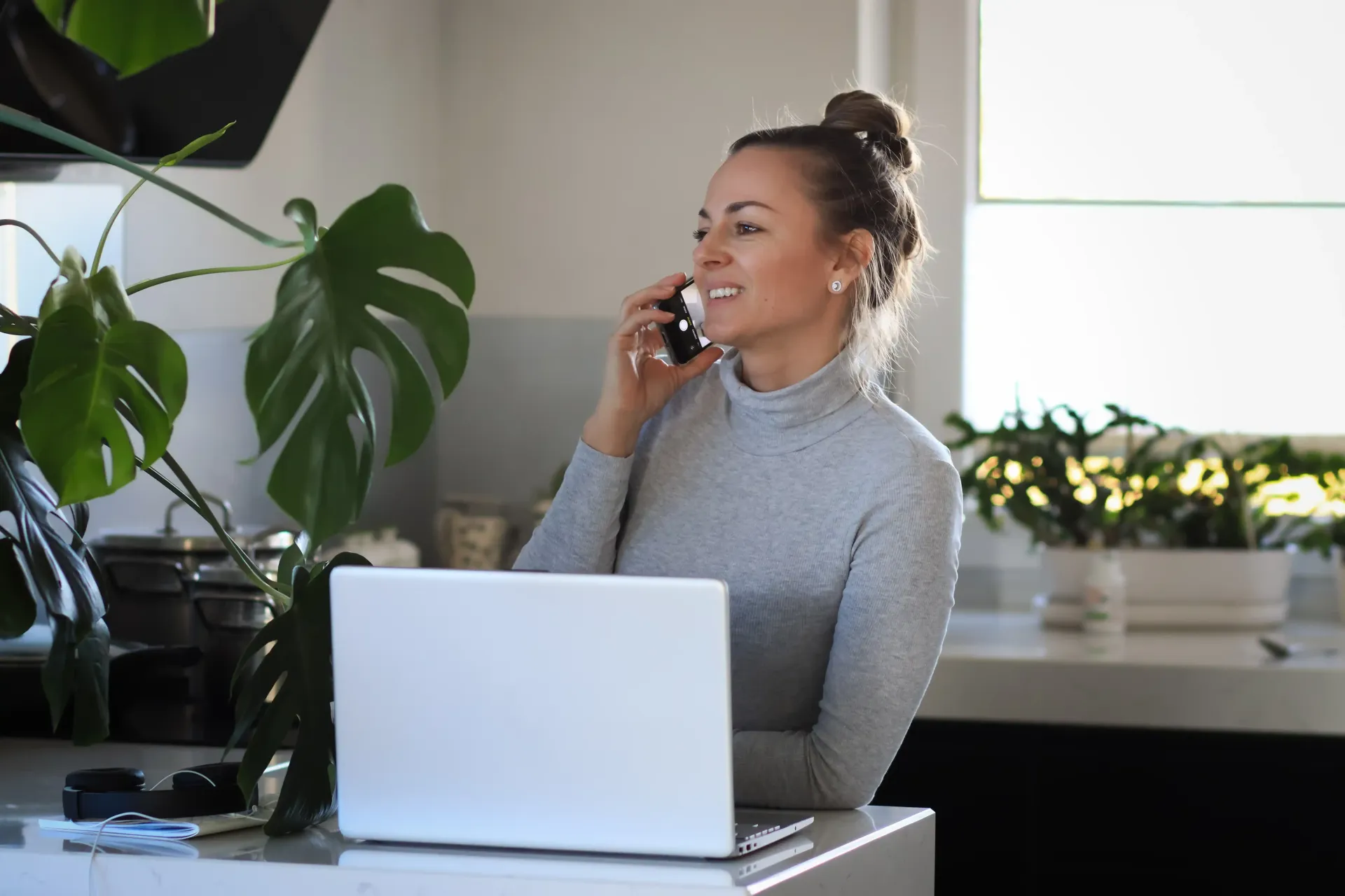 A woman is sitting in front of a laptop computer talking on a cell phone to make a new sale in her coaching business without launching new products.
