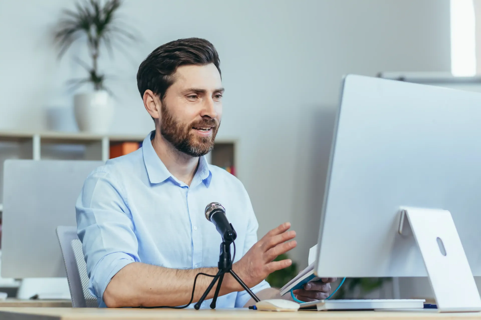 A man is sitting at a desk in front of a computer and talking into a microphone teaching a masterclass.
