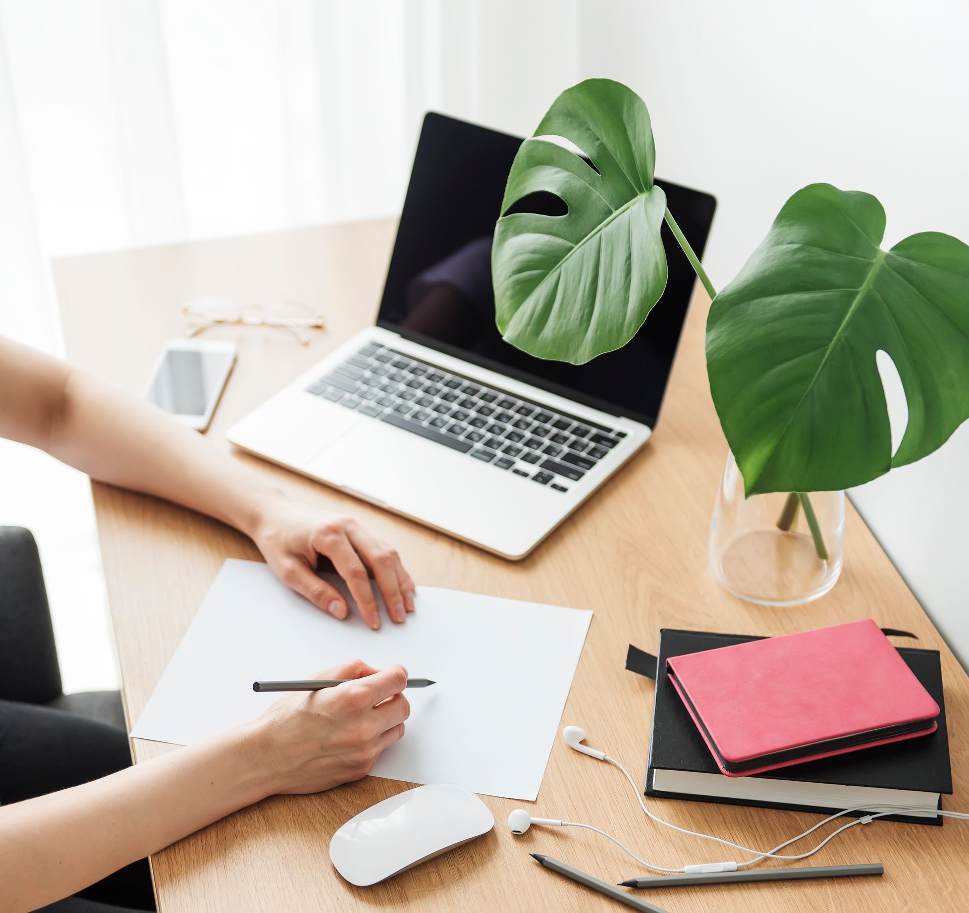 A person is writing on a piece of paper in front of a laptop computer brainstorming how they can use AI for their coaching business.