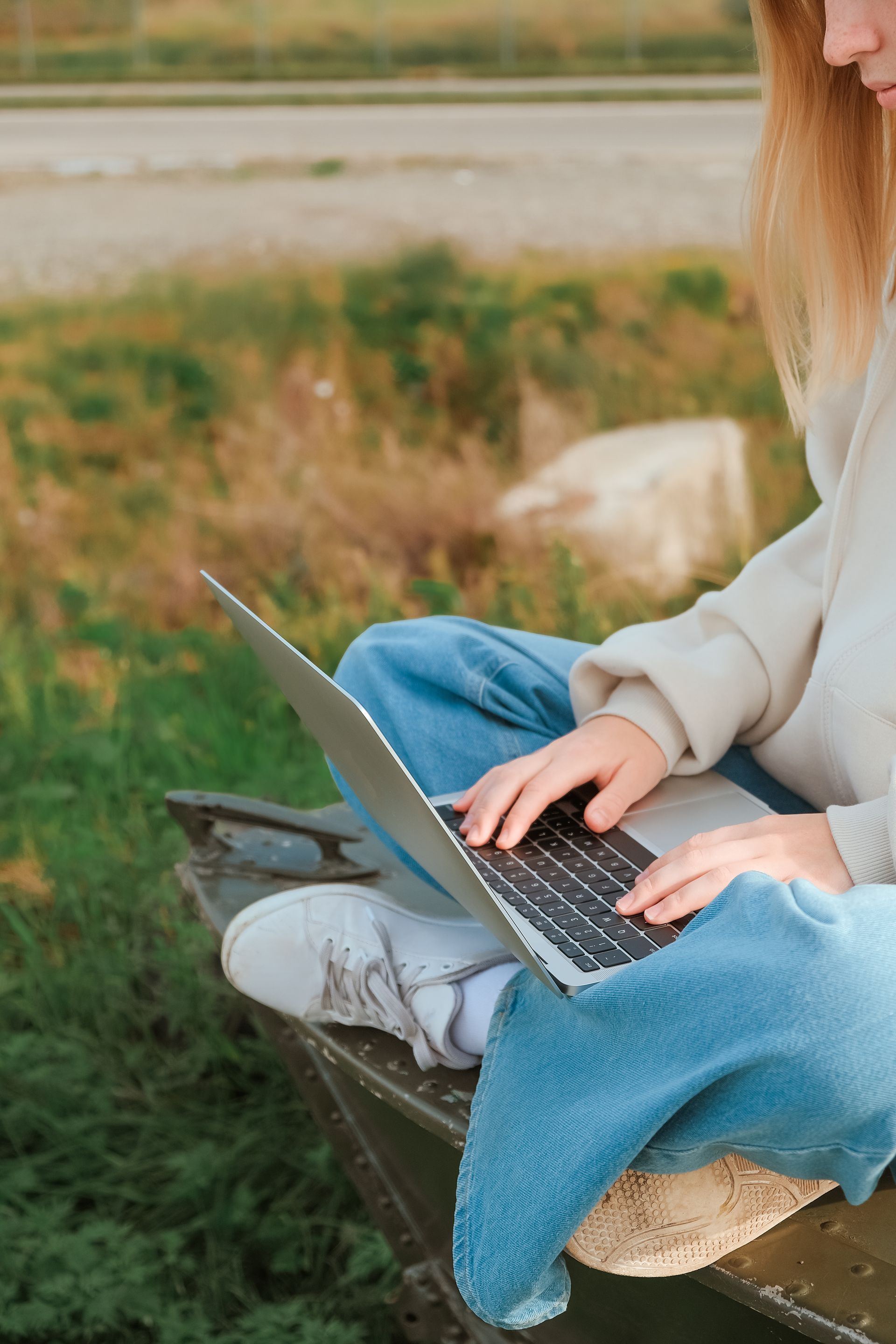 A woman is sitting on a bench using a laptop computer to create evergreen content.