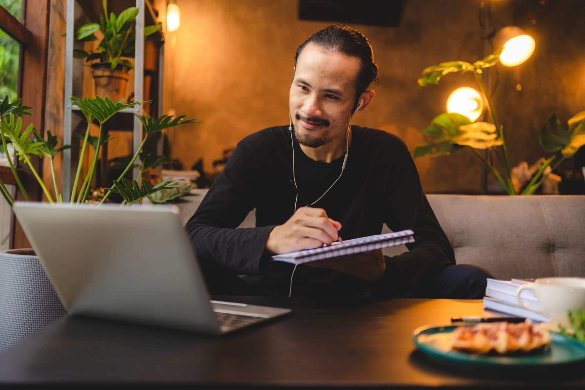 A man is sitting at a table with a laptop and a notebook learning from AP Digital Service on how to generate more revenue by blogging.