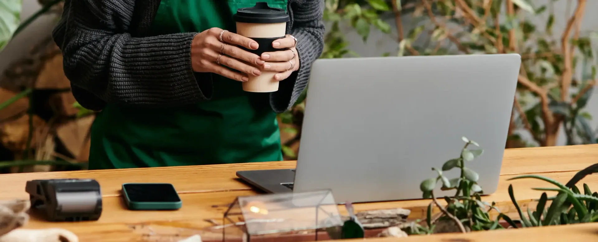 A woman is sitting at a table holding a cup of coffee and a laptop.