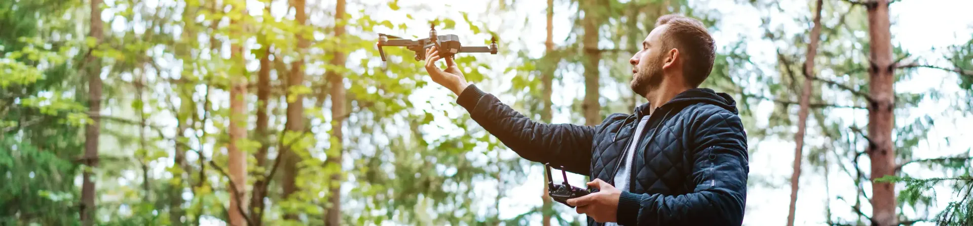 A man is flying a drone in the woods.