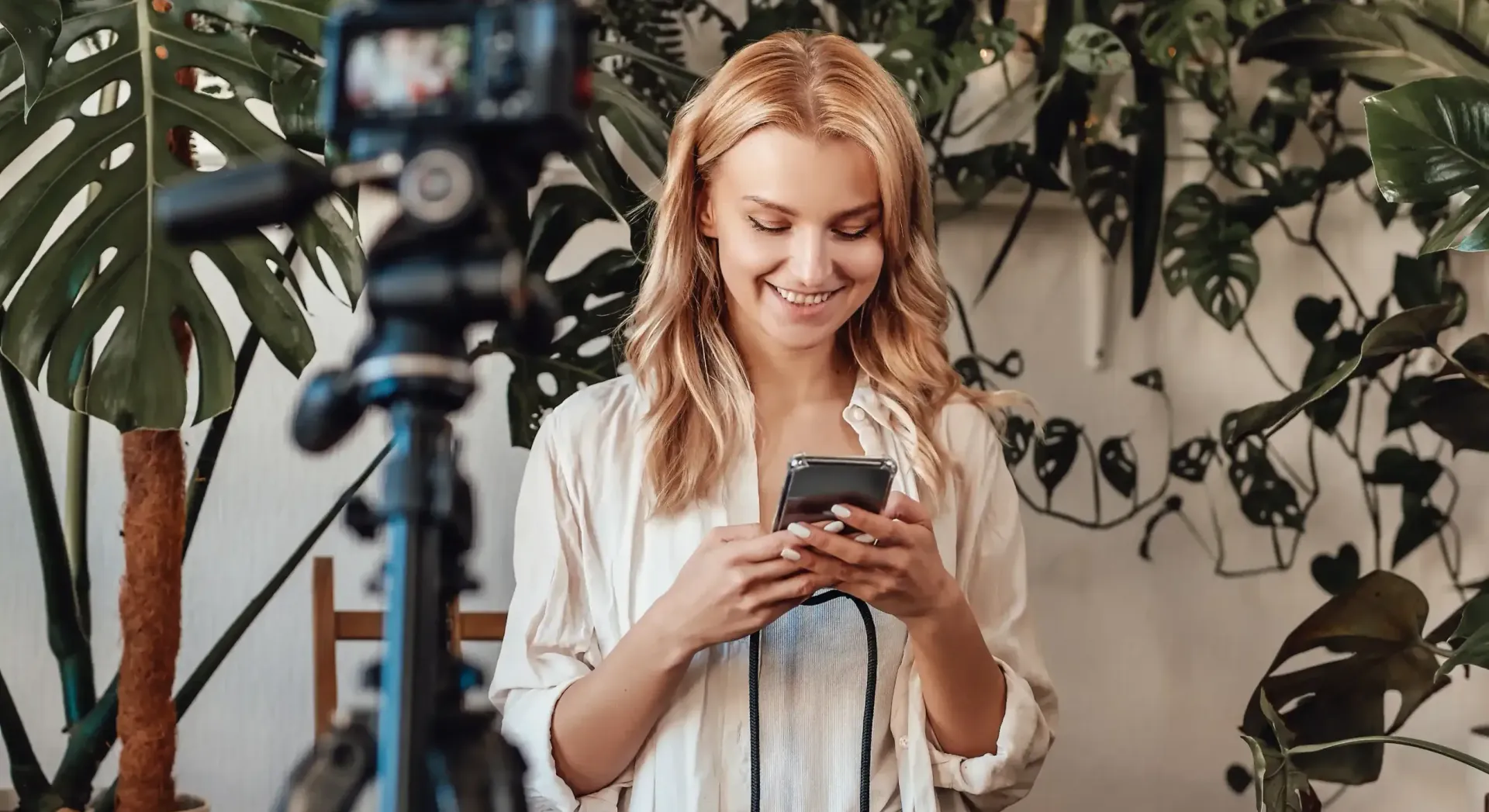 A woman is standing in front of a camera looking at her phone.