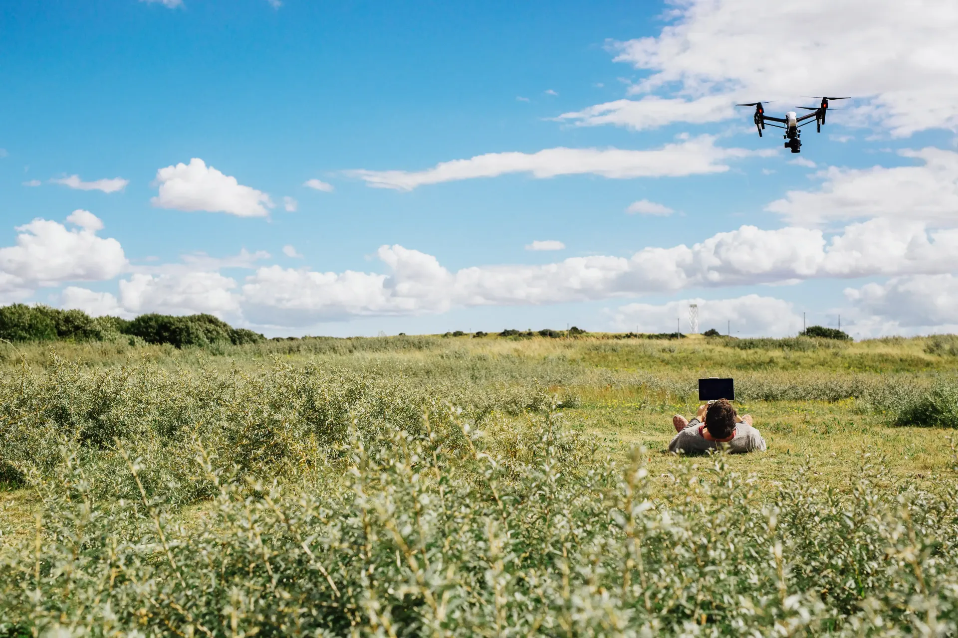 A person is sitting in a field with a drone flying overhead.