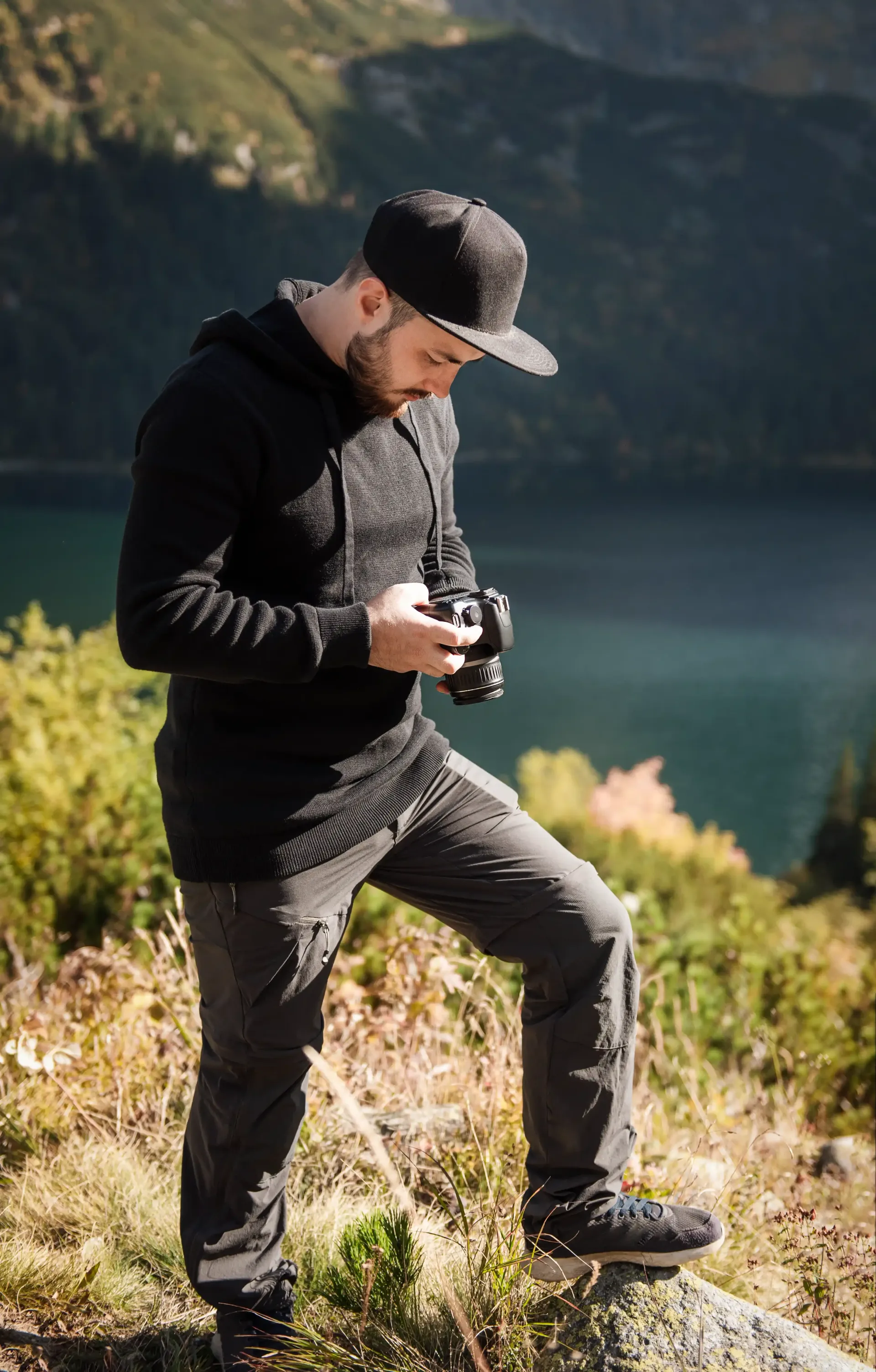 A man is standing on a rock taking a picture of a lake.