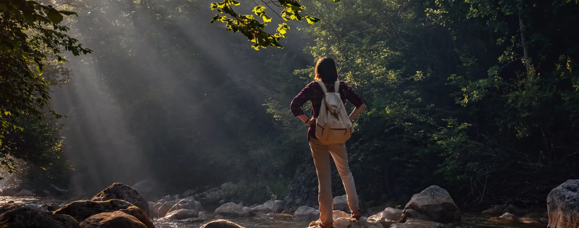 A woman with a backpack is standing in the middle of a river.