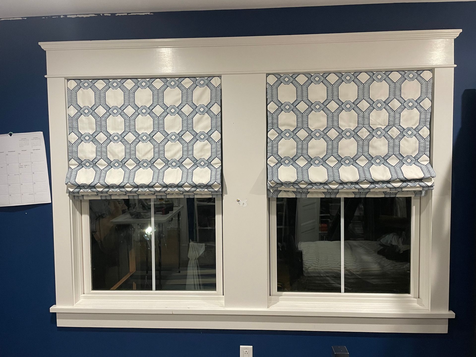 Two windows with blue and white patterned roman shades and white trim.