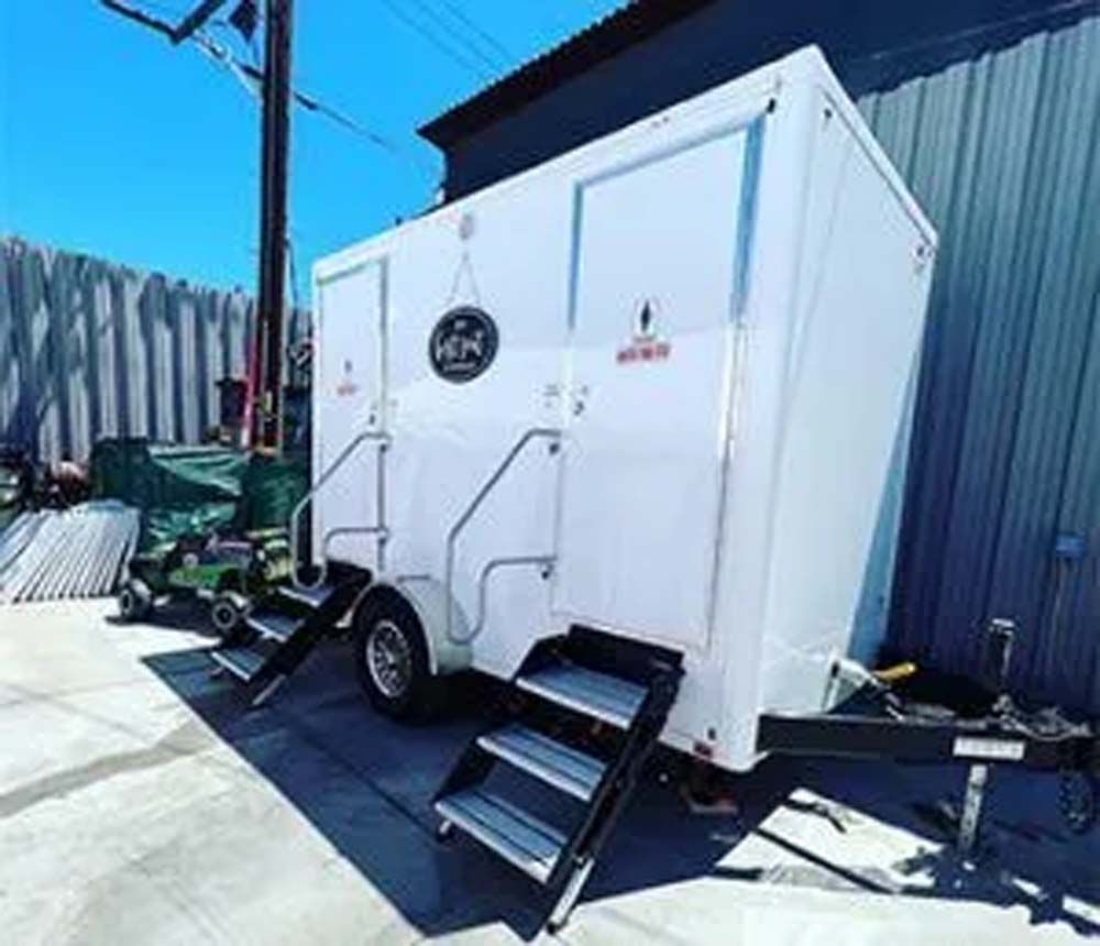 White portable restroom trailer with steps, parked on concrete.
