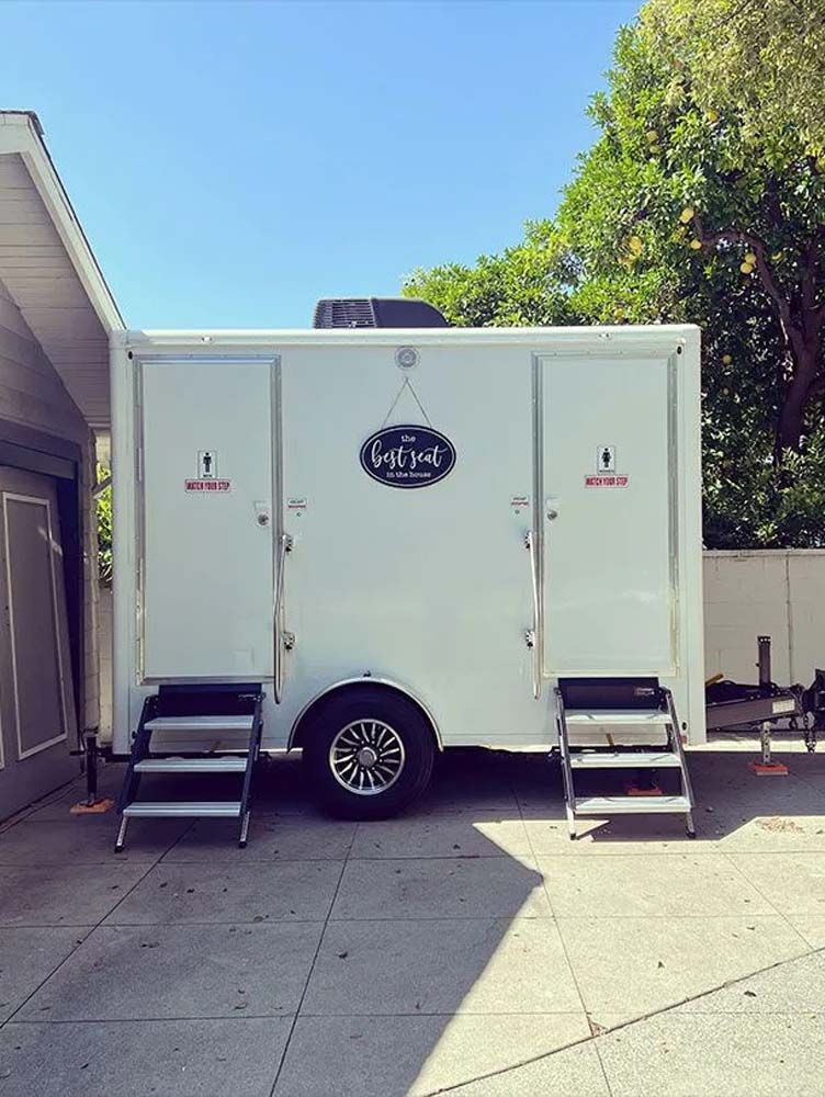 White trailer with separate entrances for men and women on a concrete surface.