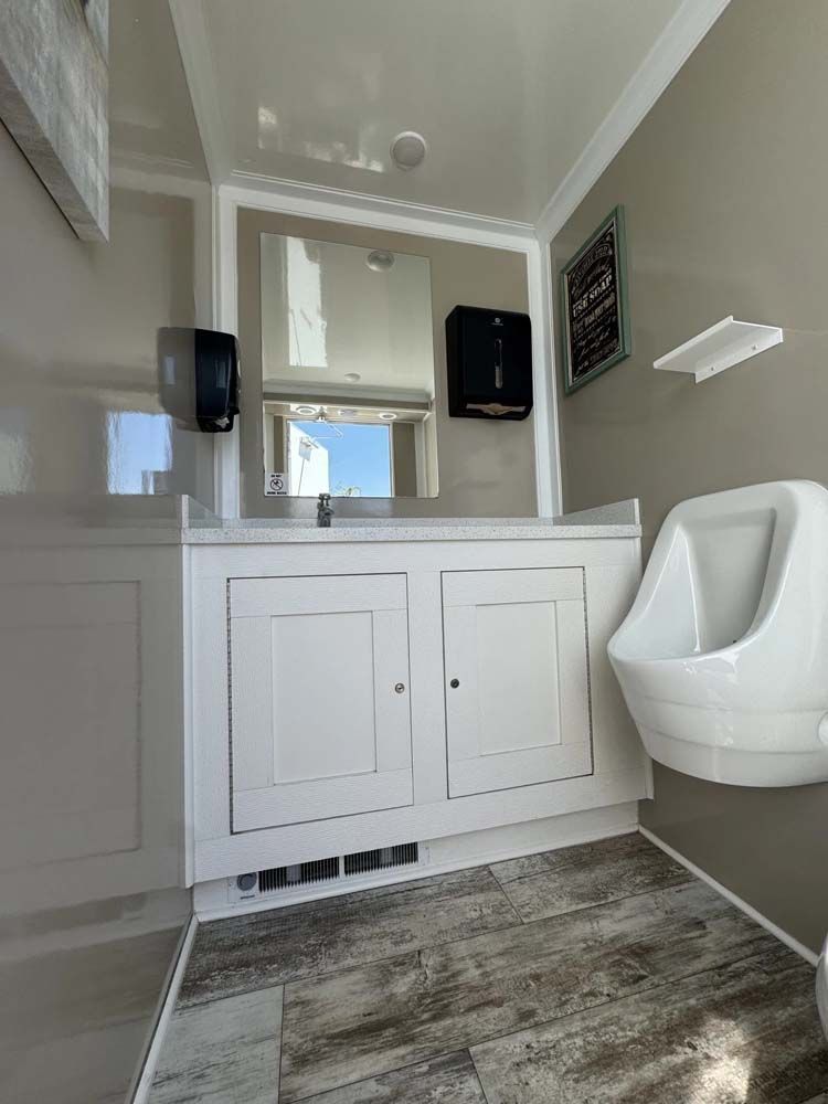 White restroom with a urinal, sink, mirror, and dispensers. Gray and white color scheme.