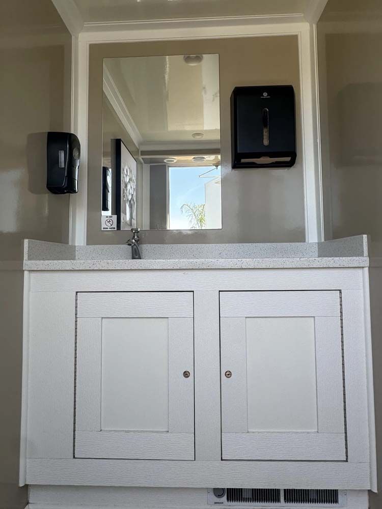A white restroom vanity with a mirror, soap dispenser, and paper towel dispenser.