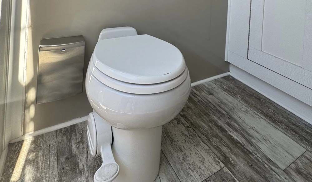 White toilet in a small bathroom with gray walls and wood-look flooring.
